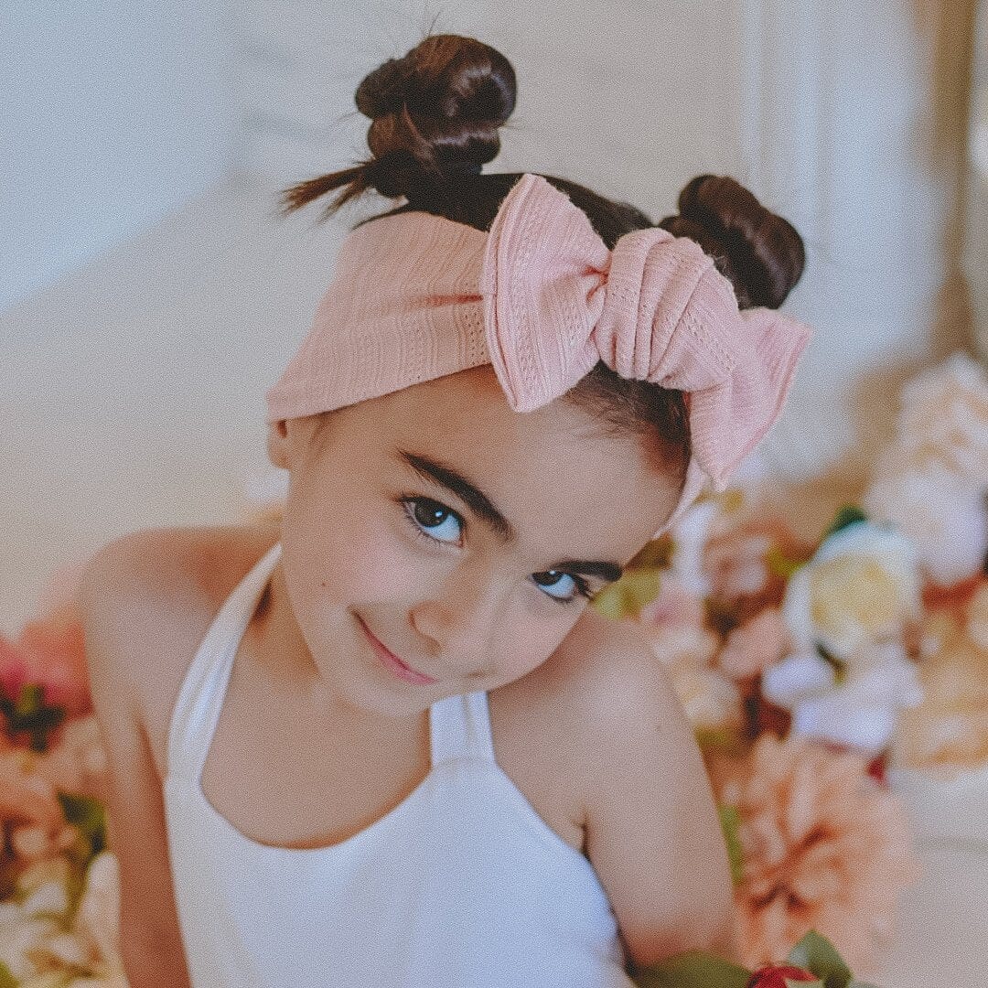 Little girl wearing a blush color headwrap with a white dress and flowers in the background